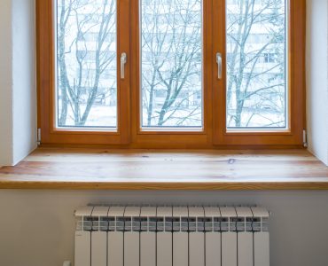 Un radiateur de chauffage placé sous une fenêtre en bois