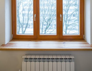Un radiateur de chauffage placé sous une fenêtre en bois