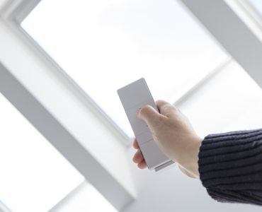 Une personne ouvre les fenêtres du toit d'une maison à l'aide d'une télécommande