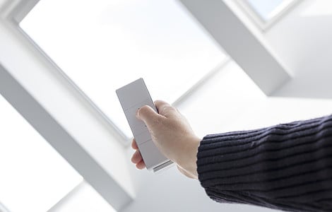 Une personne ouvre les fenêtres du toit d'une maison à l'aide d'une télécommande