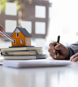 Deux hommes d'affaires signant un contrat avec une petite maquette de maison en fond
