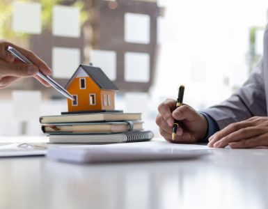 Deux hommes d'affaires signant un contrat avec une petite maquette de maison en fond