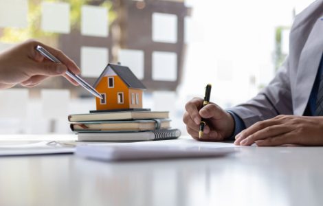 Deux hommes d'affaires signant un contrat avec une petite maquette de maison en fond