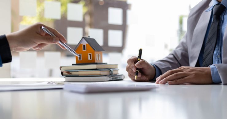 Deux hommes d'affaires signant un contrat avec une petite maquette de maison en fond