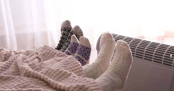 3 personnes dans le lit se réchauffent en tendant leurs pieds vers le radiateur