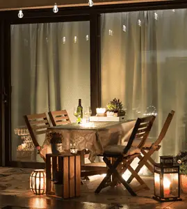 Une table à manger dressée sur la terrasse avec plusieurs lampes et ampoules allumées