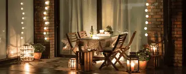 Une table à manger dressée sur la terrasse avec plusieurs lampes et ampoules allumées