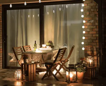 Une table à manger dressée sur la terrasse avec plusieurs lampes et ampoules allumées