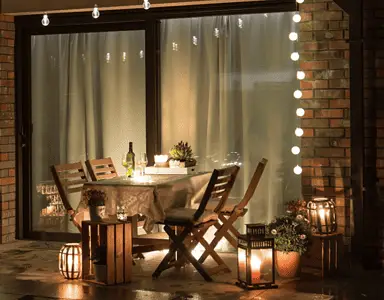 Une table à manger dressée sur la terrasse avec plusieurs lampes et ampoules allumées