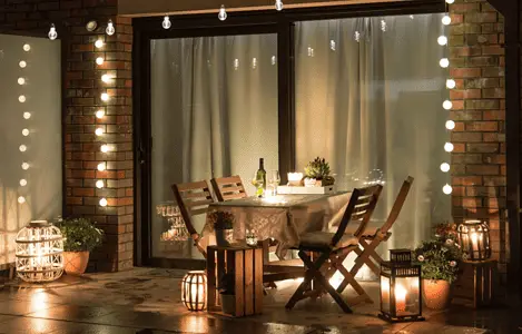 Une table à manger dressée sur la terrasse avec plusieurs lampes et ampoules allumées