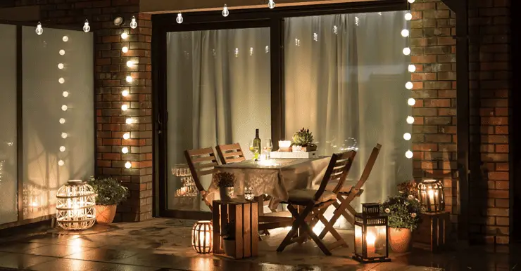 Une table à manger dressée sur la terrasse avec plusieurs lampes et ampoules allumées