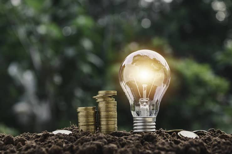 Illustration d'économie d'énergie avec une ampoule plantée dans le sol, proche des pièces de monnaies empilées
