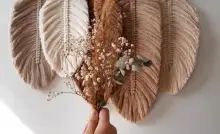 Vue sur une déco murale DIY avec une main de femme tenant un petit bouquet de fleurs
