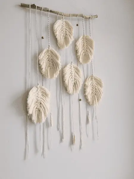 Une déco murale décorative avec des plumes en macramé et une branche en bois