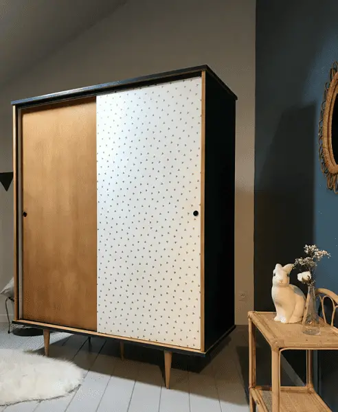Une armoire en bois vintage, tapissé d'un papier peint à petits motifs géométriques sur une seule porte 